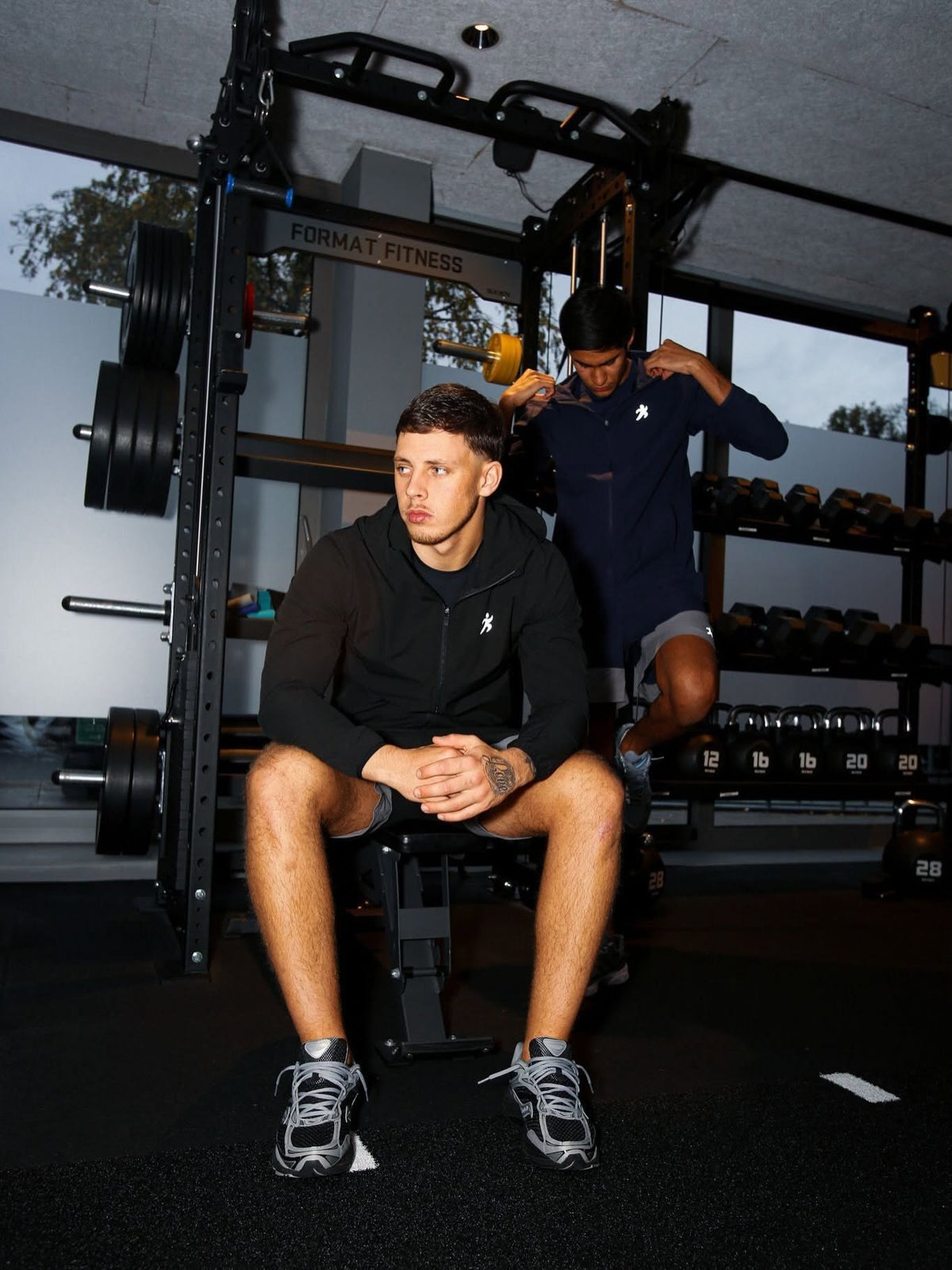Two men in training jackets and shorts in the gym